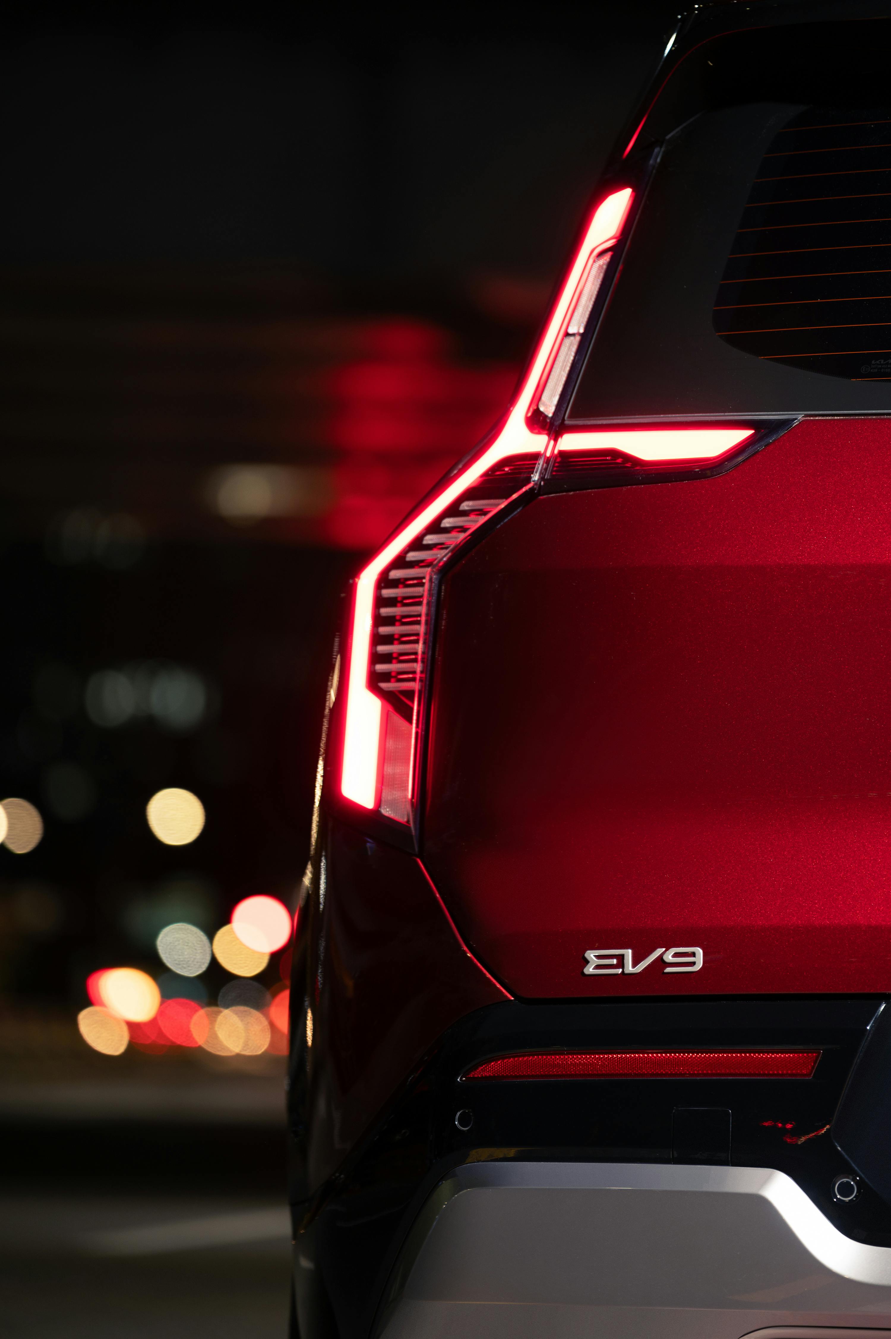 Modern EV9 SUV with sleek red design and illuminated tail lights on city street.